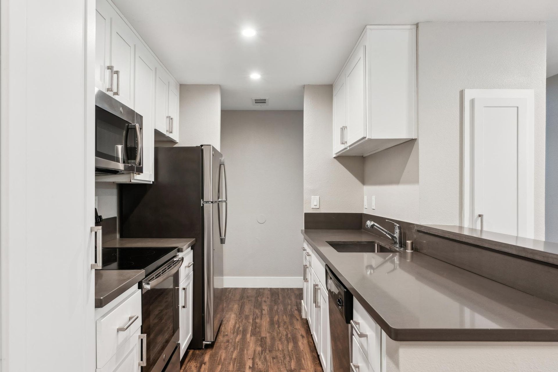 Kitchen in a modern apartment with white cabinets, stainless steel appliances, and gray countertops.