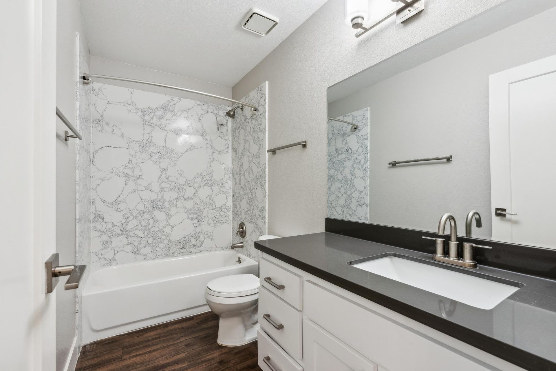 Bathroom featuring a marble-pattern shower surround, white vanity, and toilet.