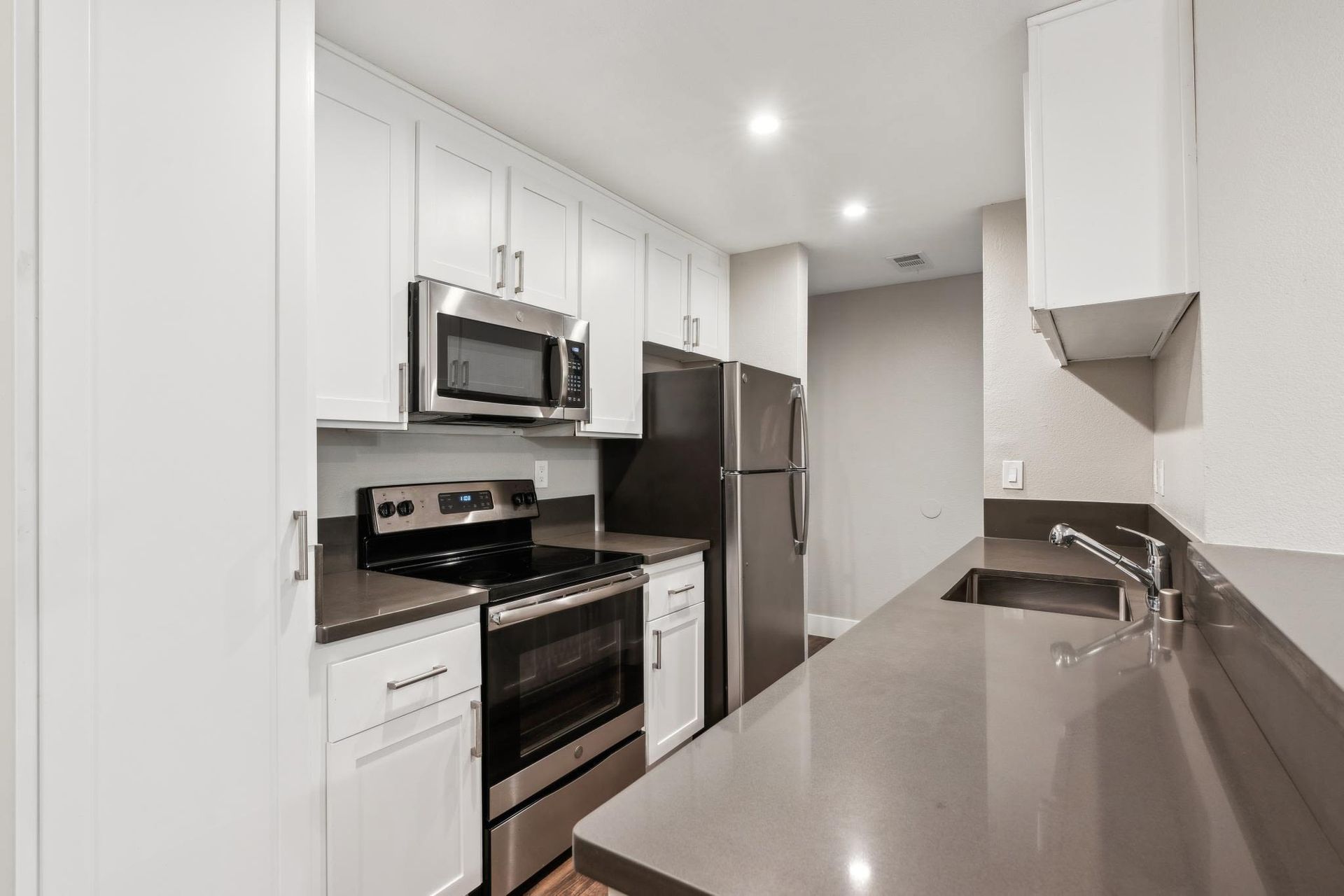 Modern white kitchen with stainless steel appliances and a long gray countertop.