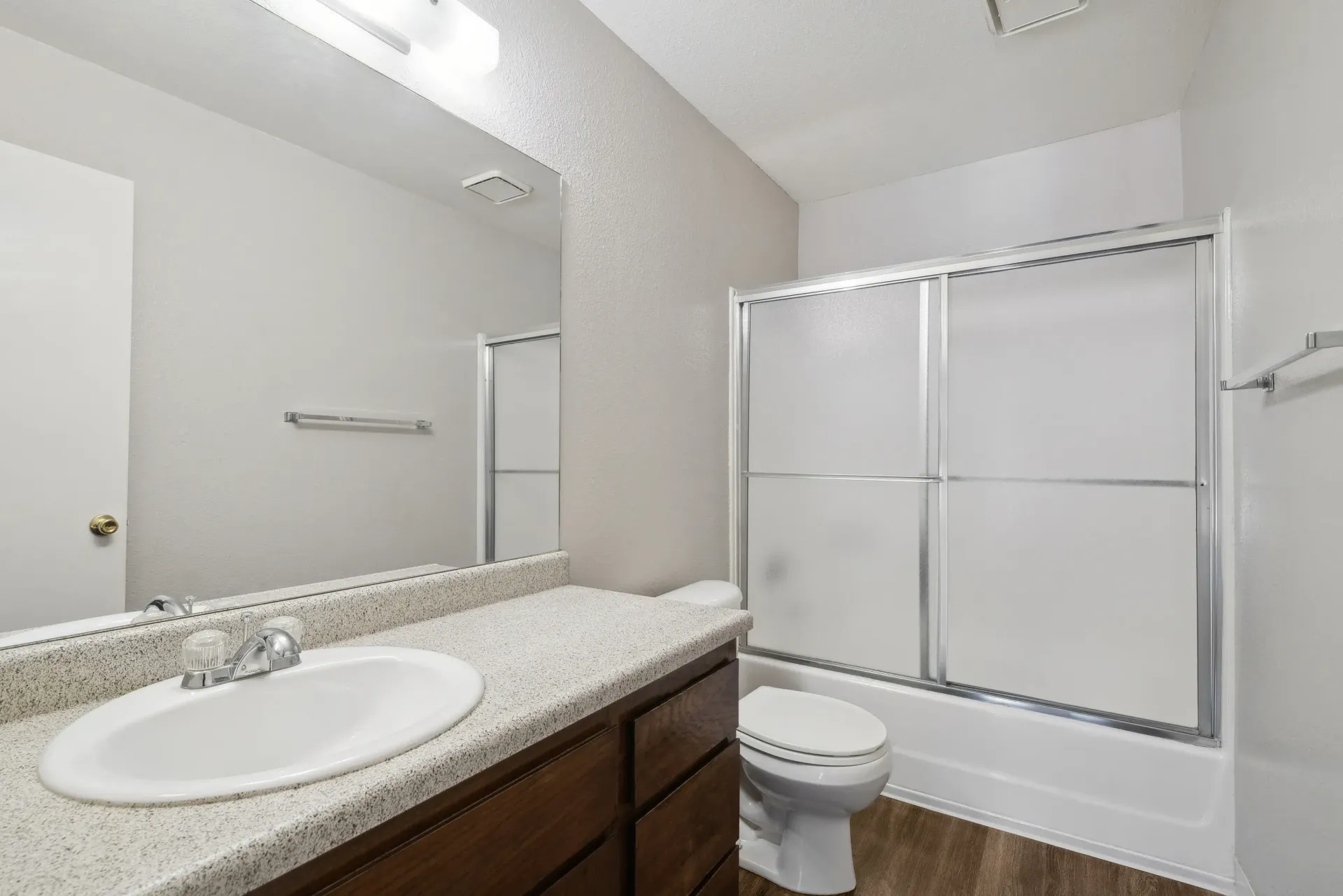 Bathroom in an apartment with a single sink vanity, mirror, toilet, and frosted glass sliding tub/shower.