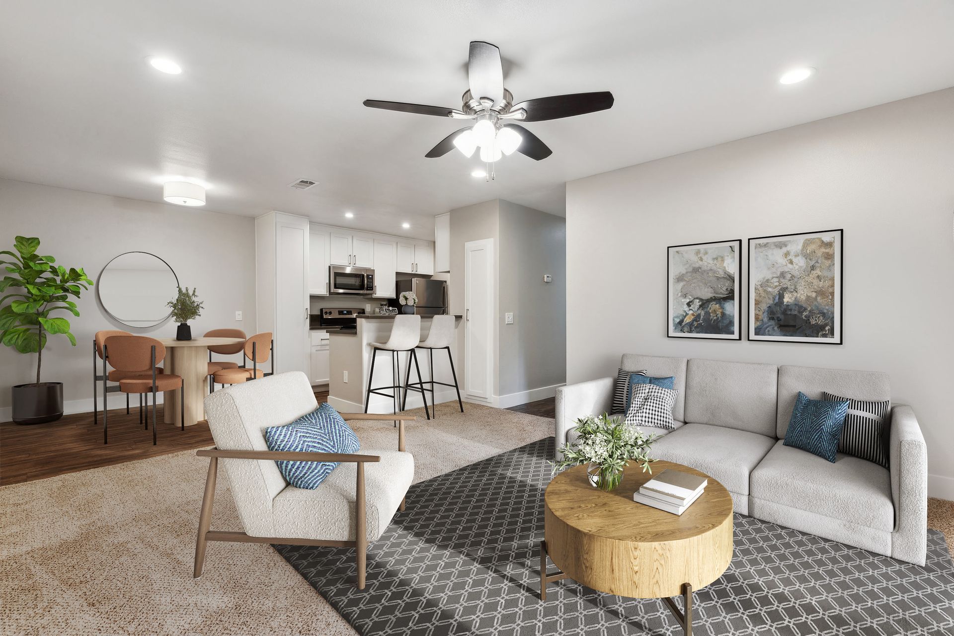 Open-concept living room with sofa, armchair, round coffee table, dining area, and kitchen in the background.