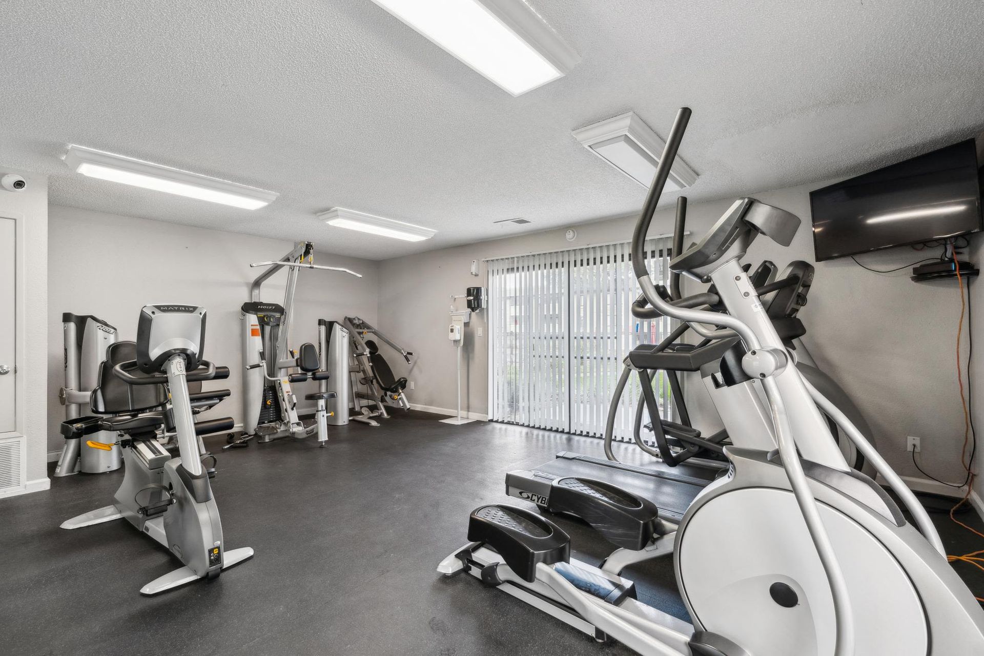 Indoor fitness center with treadmills, ellipticals, weights, and a wall-mounted TV.
