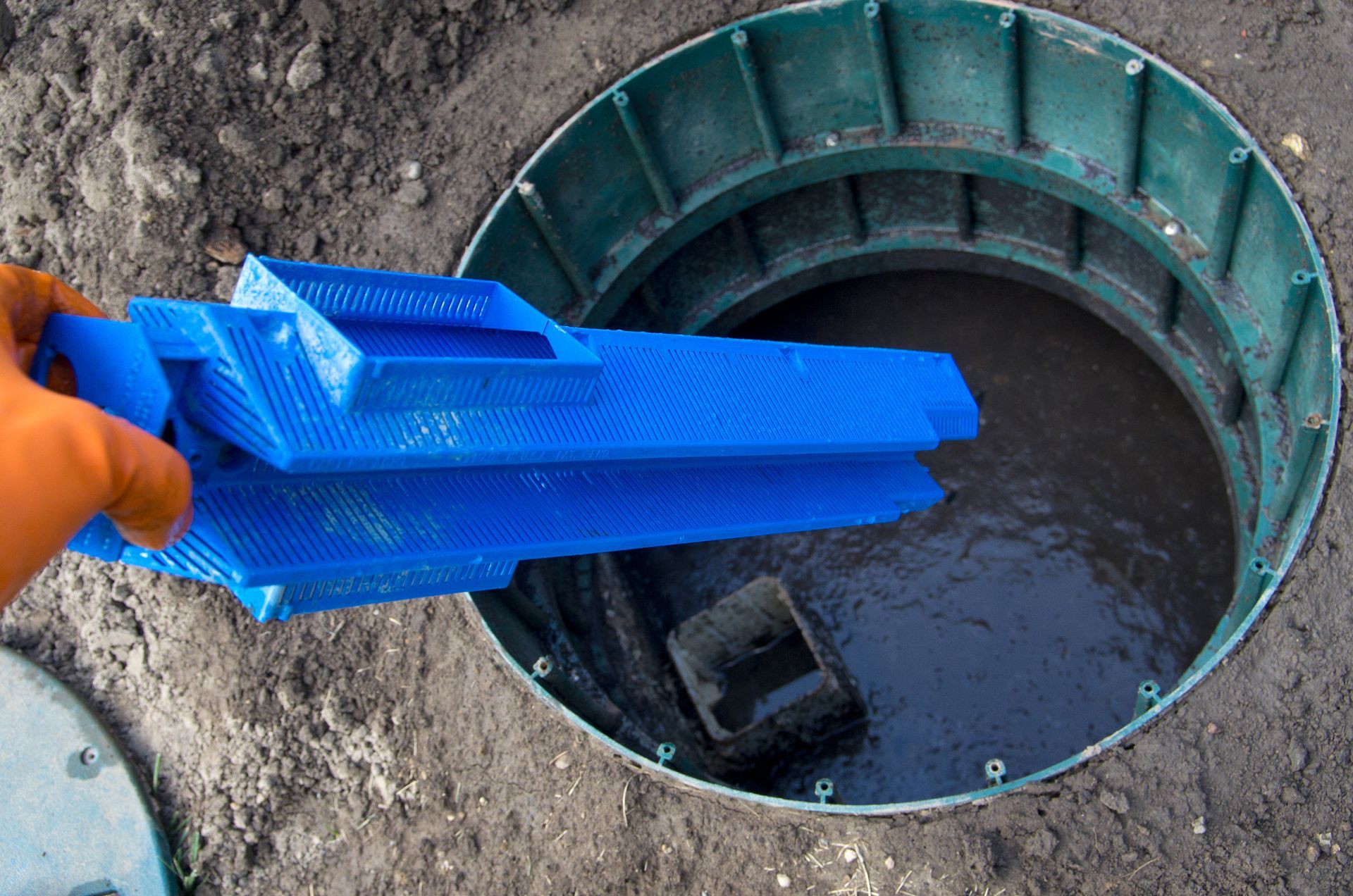 A person is holding a blue object in a hole in the ground.