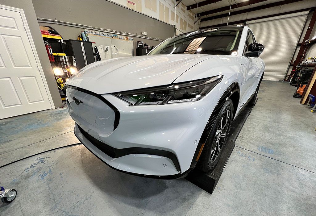 White Ford Mustang Mach-E electric SUV parked inside a garage. Black accents and wheels.