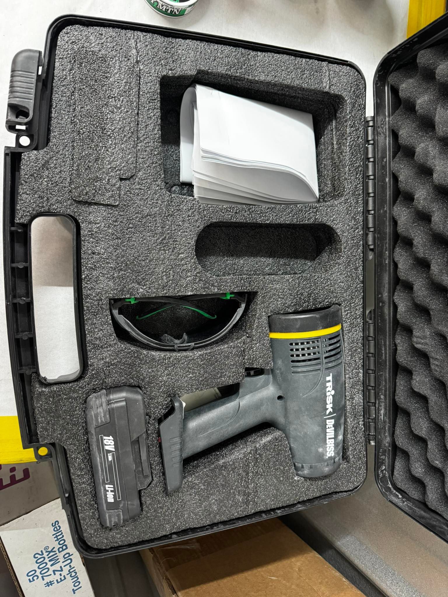 A gray heat gun, battery, and safety glasses stored in a protective carrying case with foam inserts.