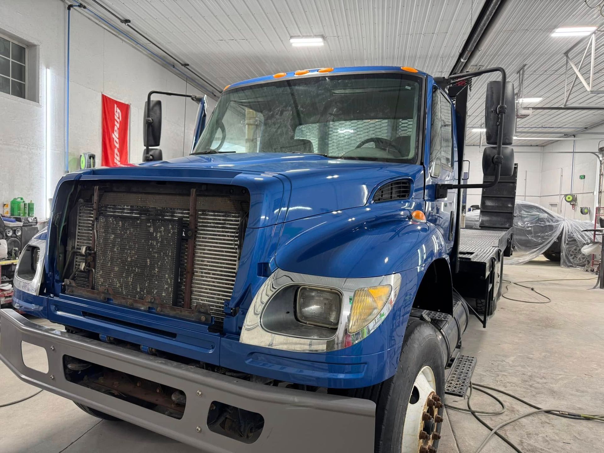 A blue Freightliner truck in a garage with its front grille and headlight housing removed.