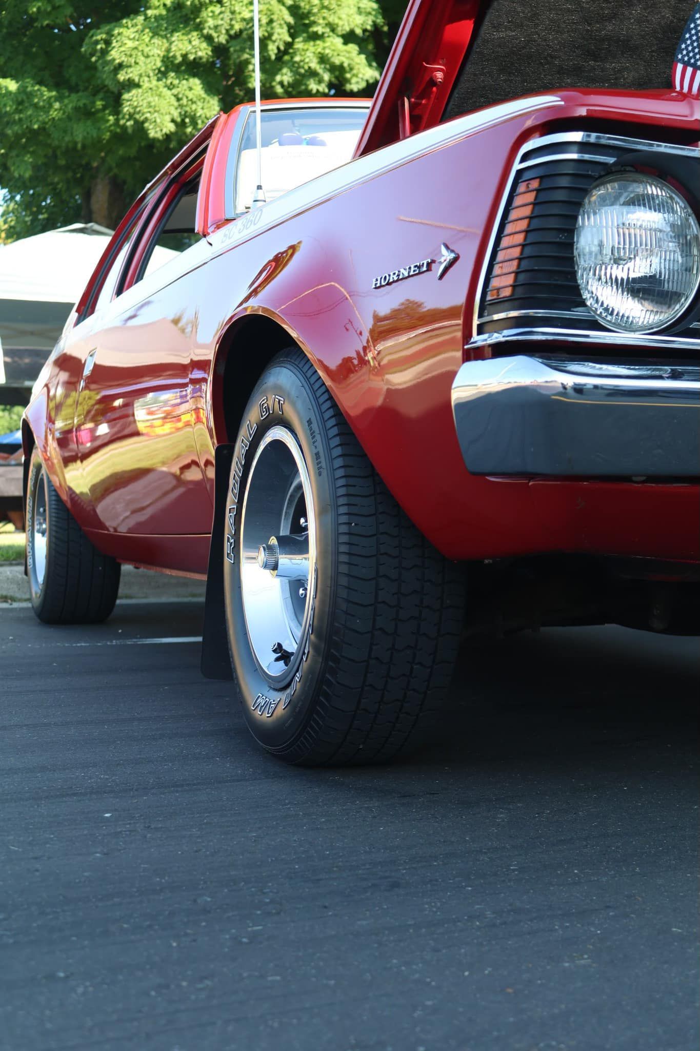 A low-angle view of a shiny red classic car parked outdoors with its hood open.