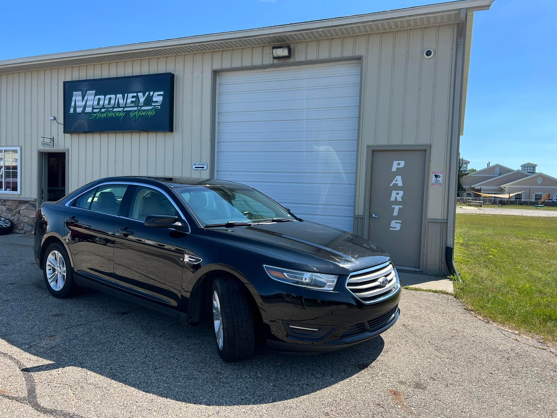 A black sedan parked in front of a metal-sided building with a 