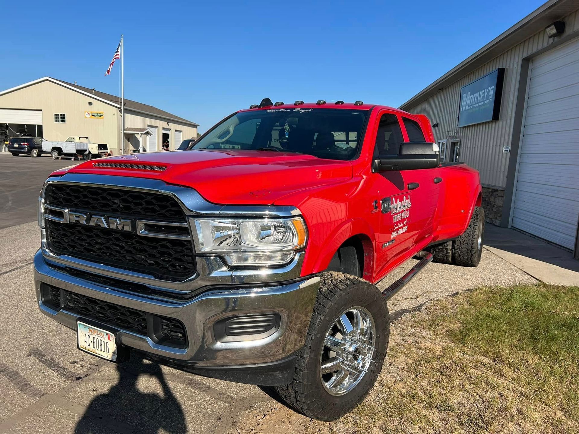 A bright red, dual-rear-wheel Ram pickup truck parked in front of a commercial building on a sunny day.