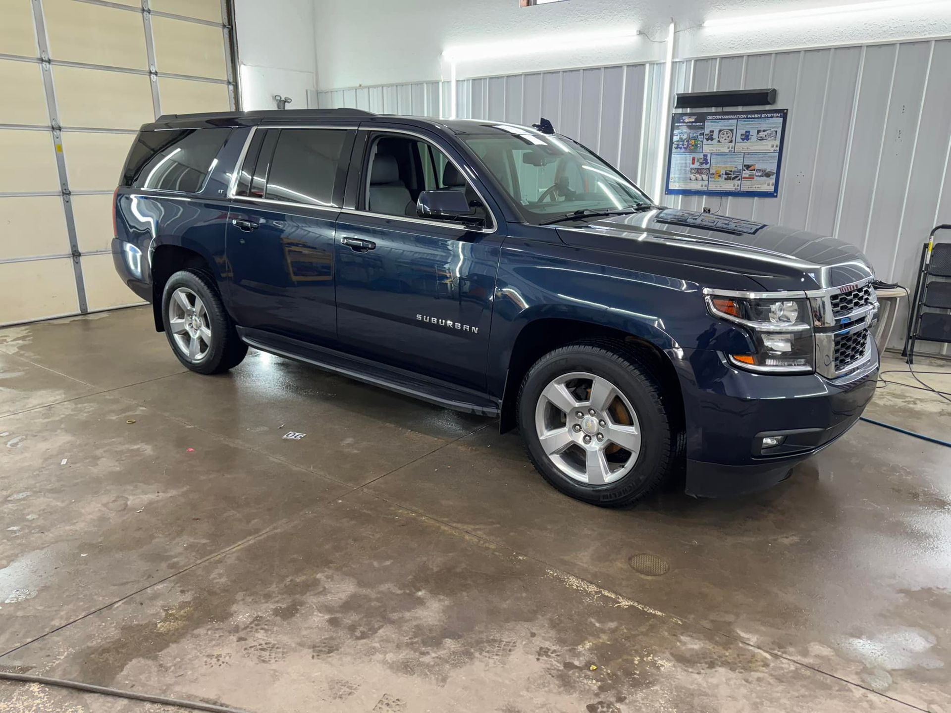 A dark blue Chevrolet Suburban SUV parked inside a bright, clean garage with a concrete floor.