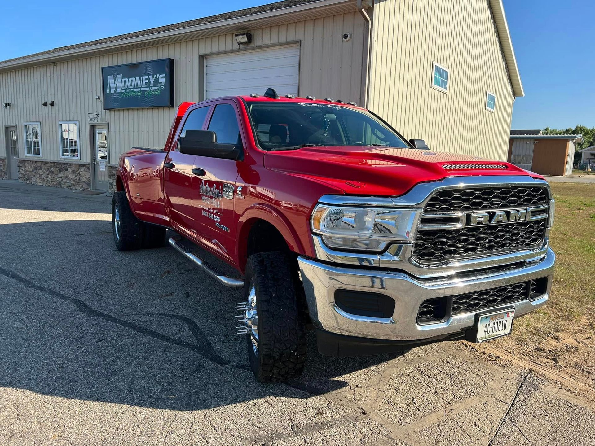 A bright red Ram dually pickup truck parked on an asphalt lot in front of a metal-sided commercial building.