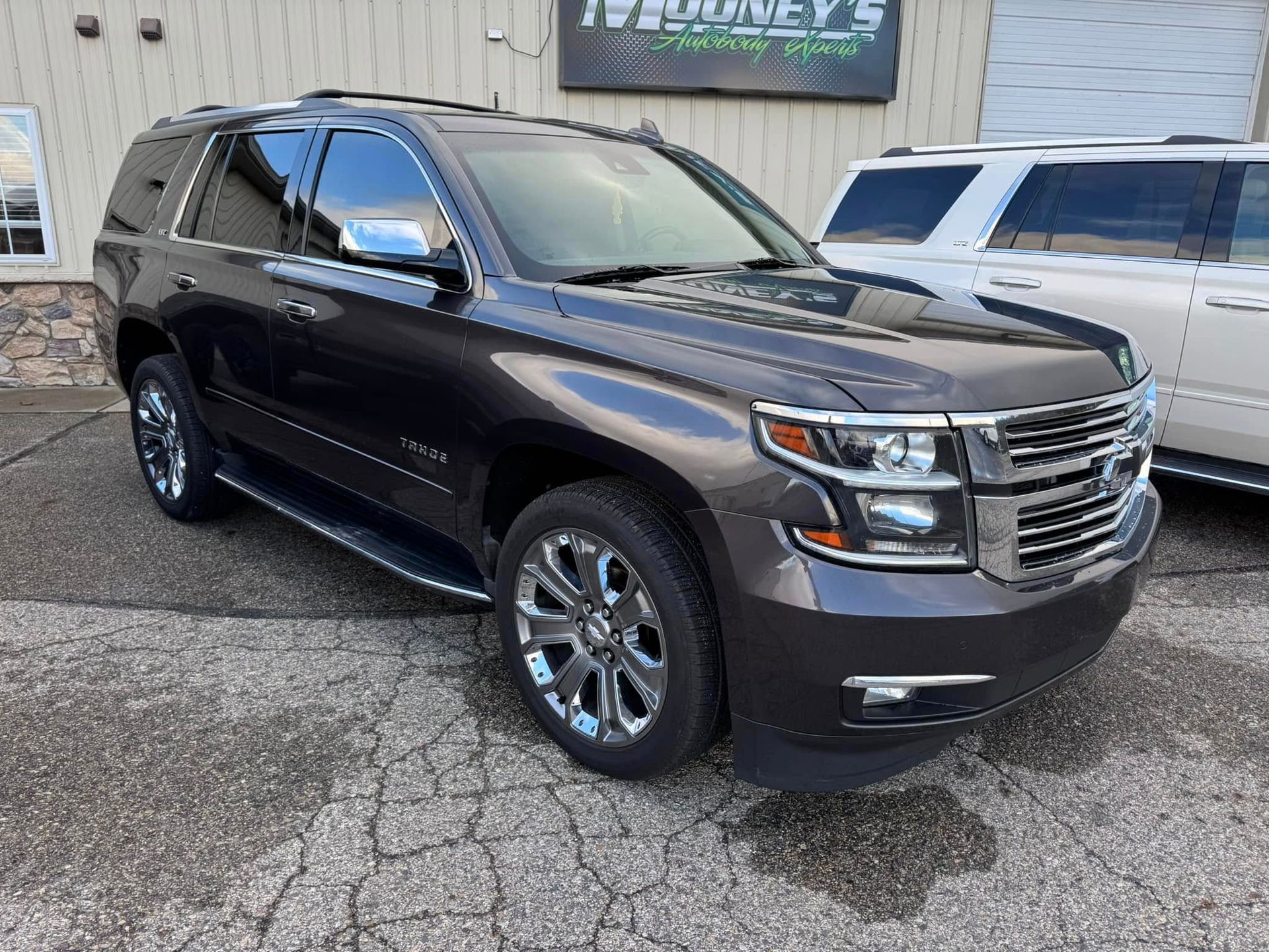 A dark brown Chevrolet Tahoe SUV parked on a paved lot with another white SUV visible in the background.