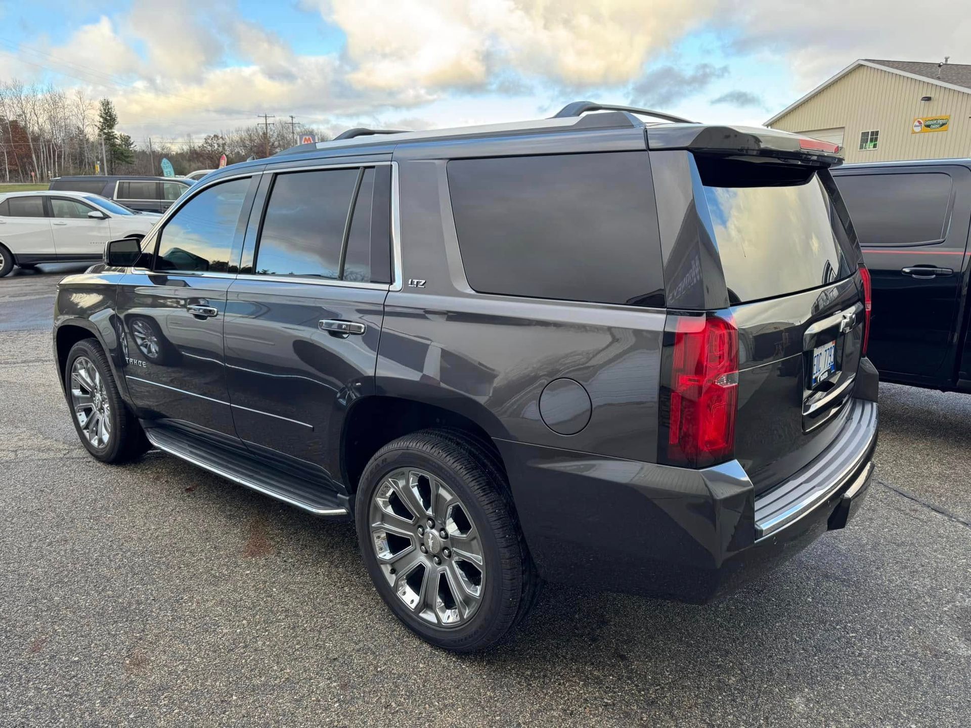 A dark gray GMC Yukon SUV parked on an asphalt lot under a cloudy sky.