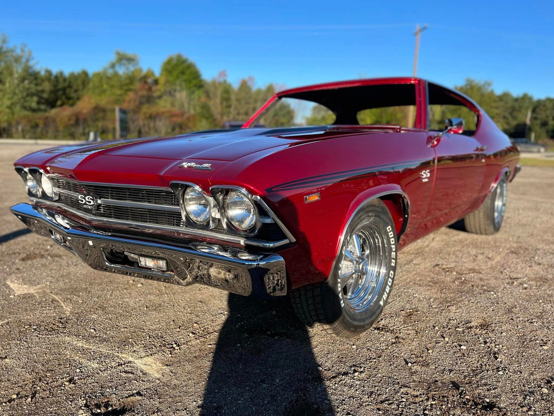 A deep red 1969 Chevrolet Chevelle SS parked on a gravel surface under a clear blue sky.