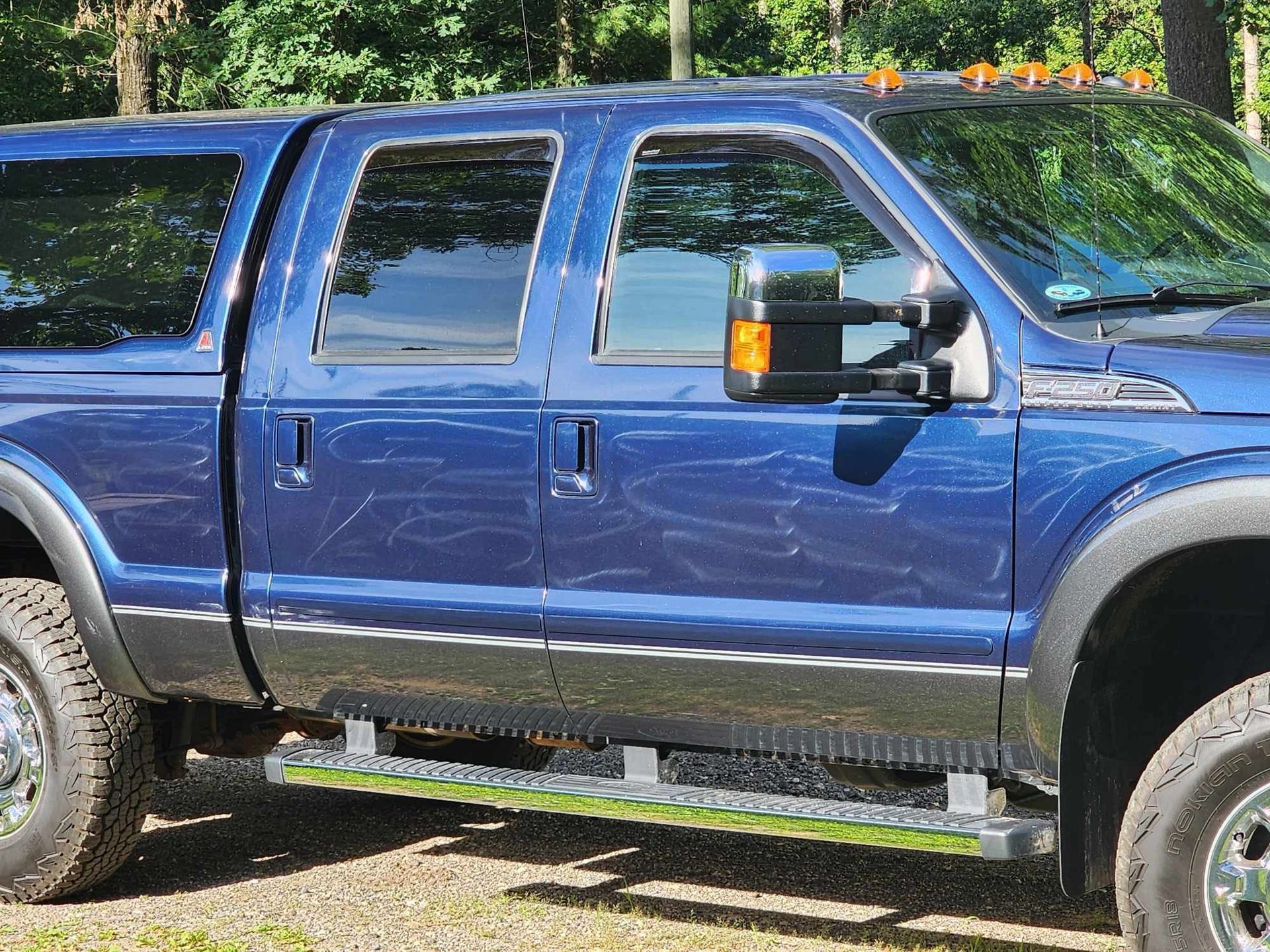 A side view of a blue crew cab pickup truck with a camper shell parked on a gravel surface.