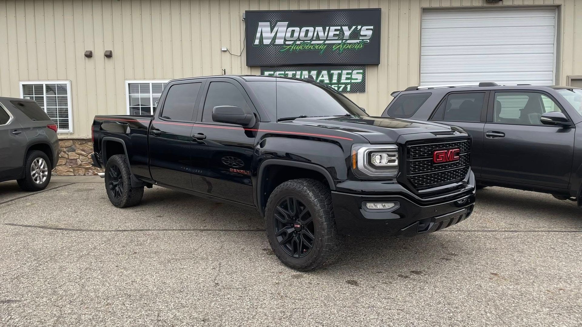 A black GMC pickup truck parked in front of an automotive shop named Mooney's.
