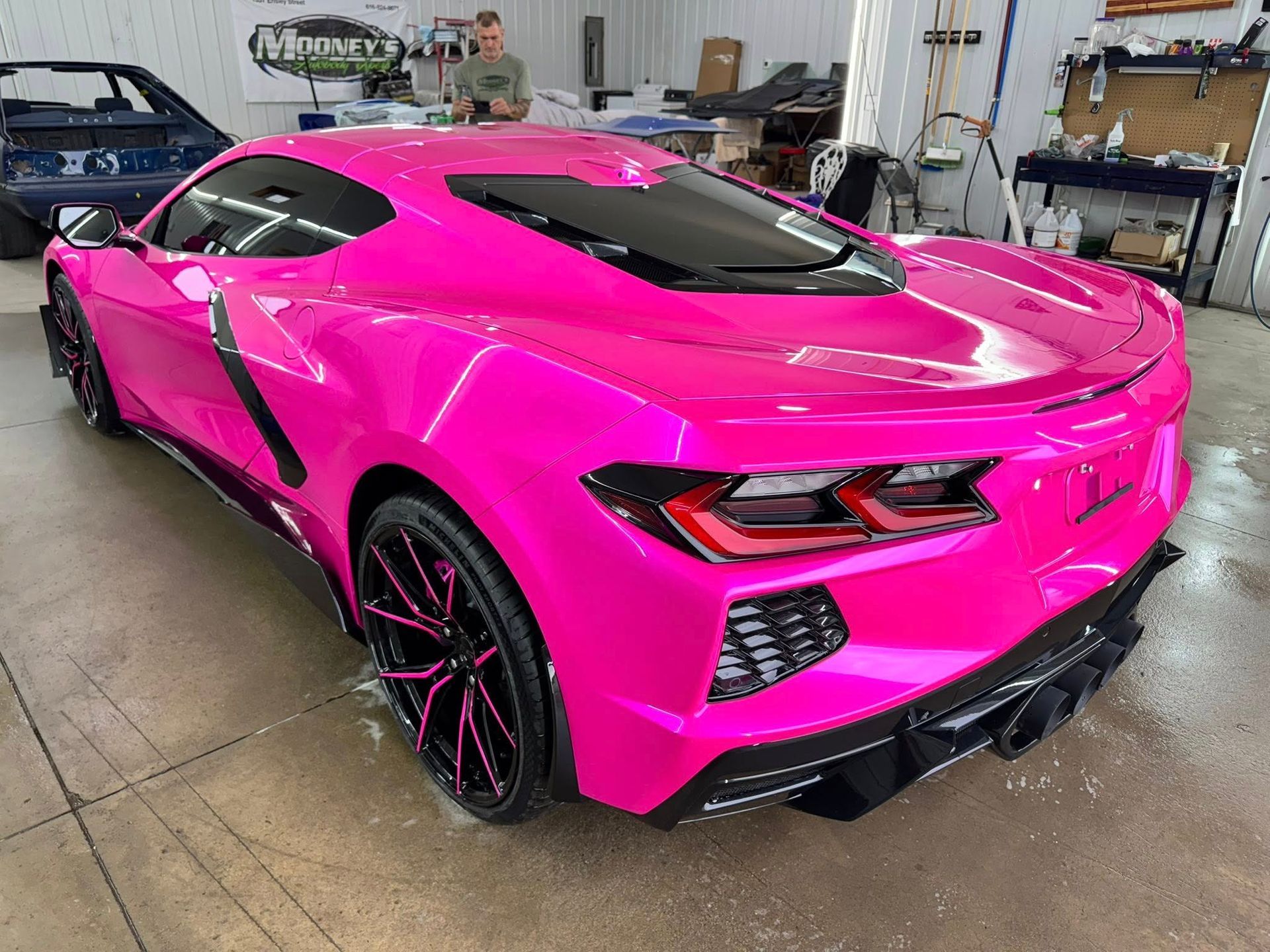 A bright pink Chevrolet Corvette parked in a garage, showcasing its rear design, black wheels, and sleek body lines.