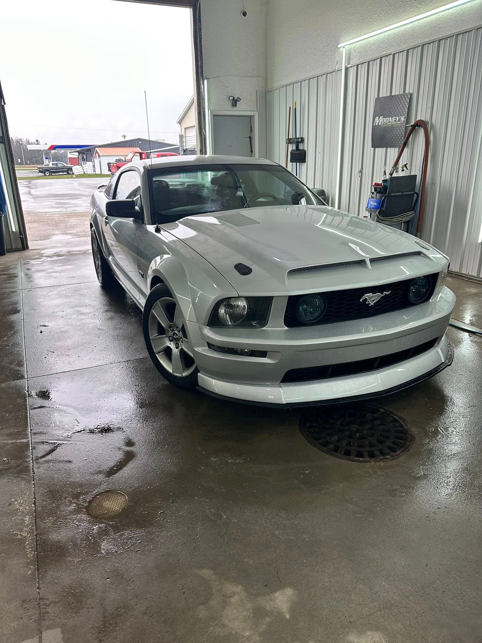 A silver Ford Mustang parked inside a garage with a wet concrete floor.