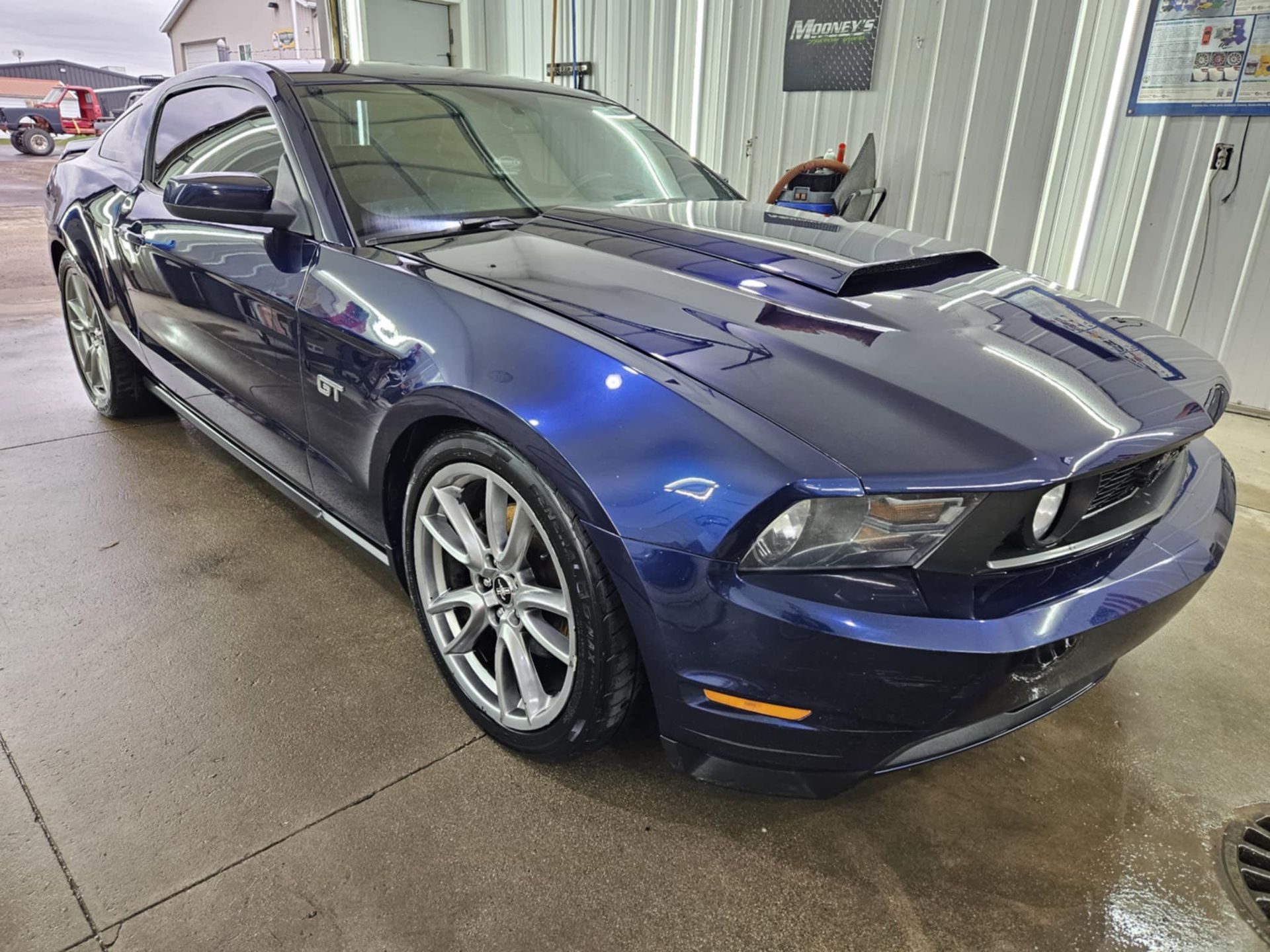 A dark blue Ford Mustang GT parked inside a garage, angled toward the front passenger side.
