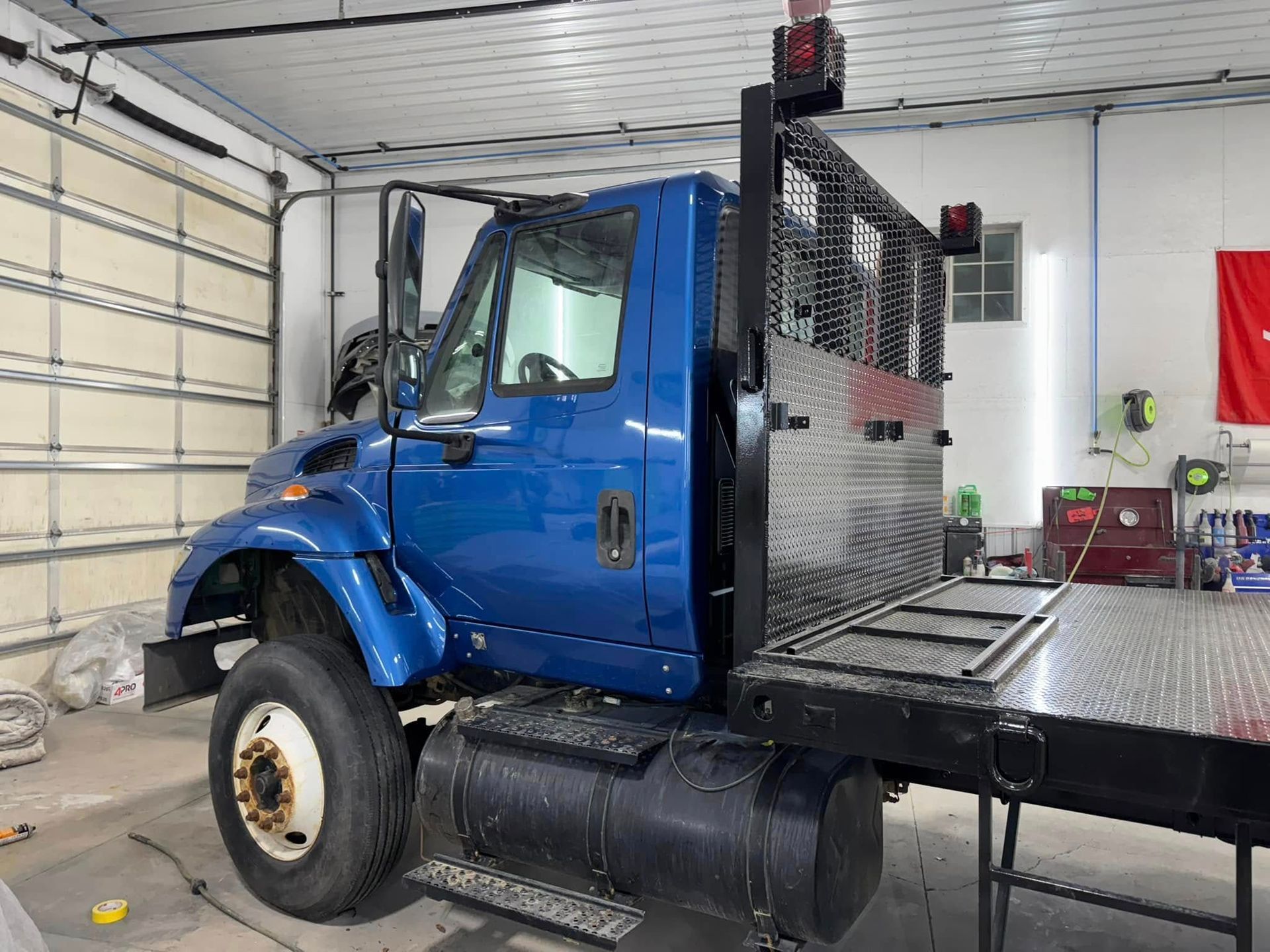 A blue commercial flatbed truck parked inside a garage workshop.