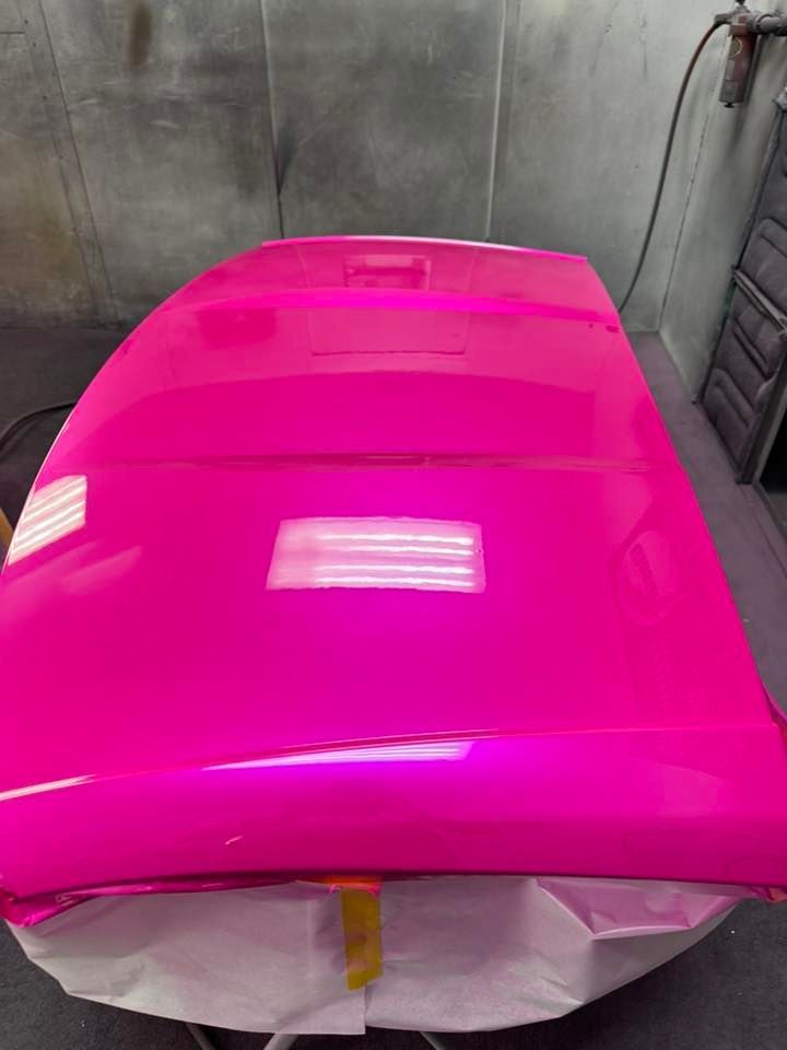 A bright, freshly painted neon pink car hood rests on a stand in a workshop.