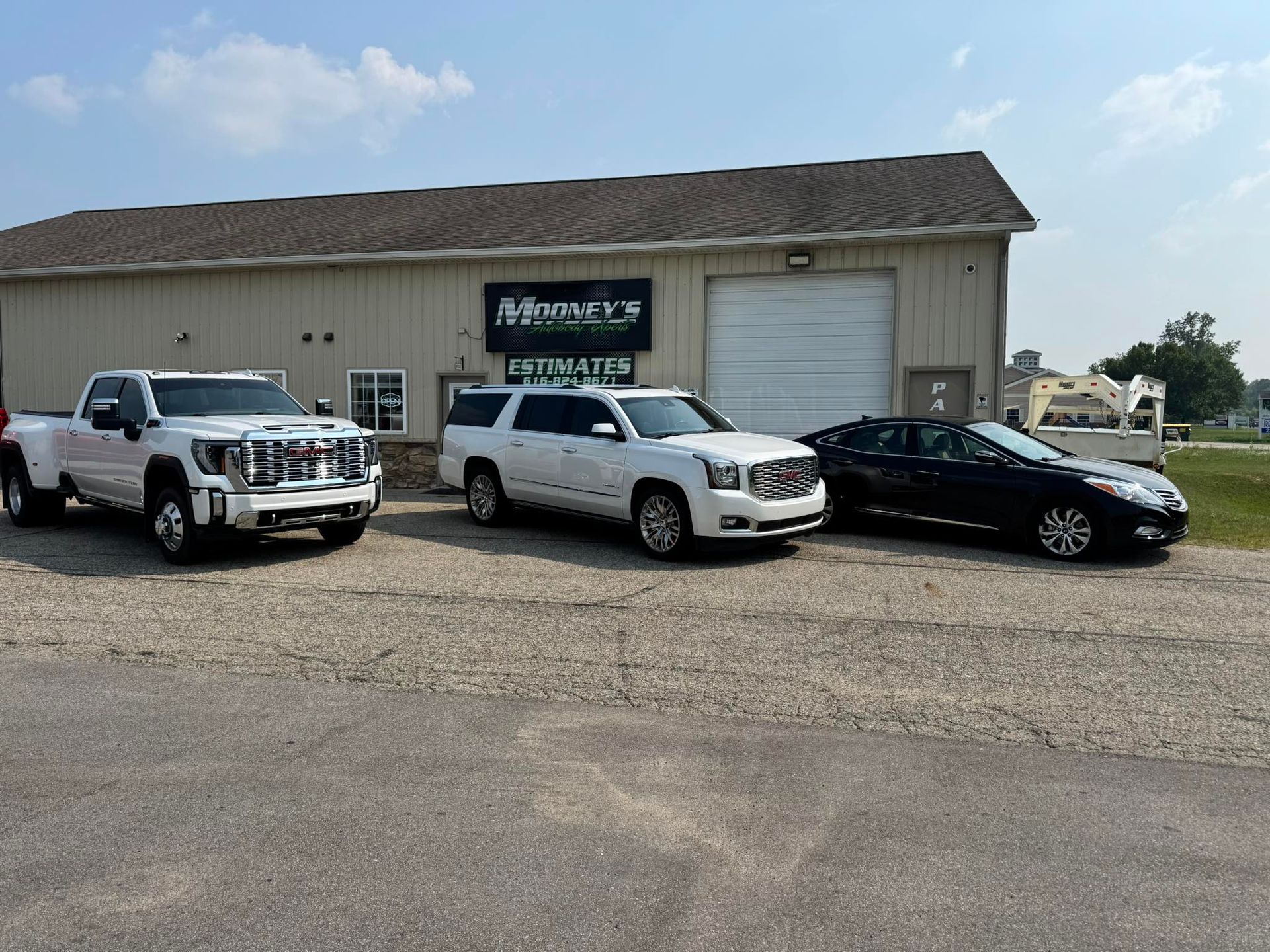 Three vehicles, including two white trucks and a black sedan, are parked in front of a light-colored commercial building.