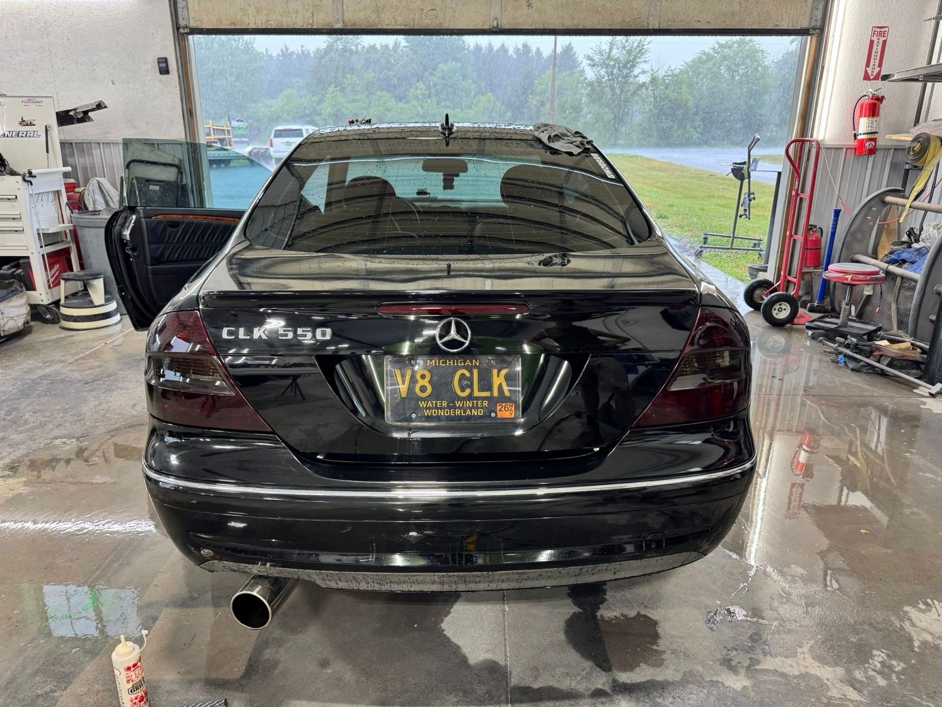 A black Mercedes-Benz CLK 550 parked inside an auto shop with a vanity plate reading 