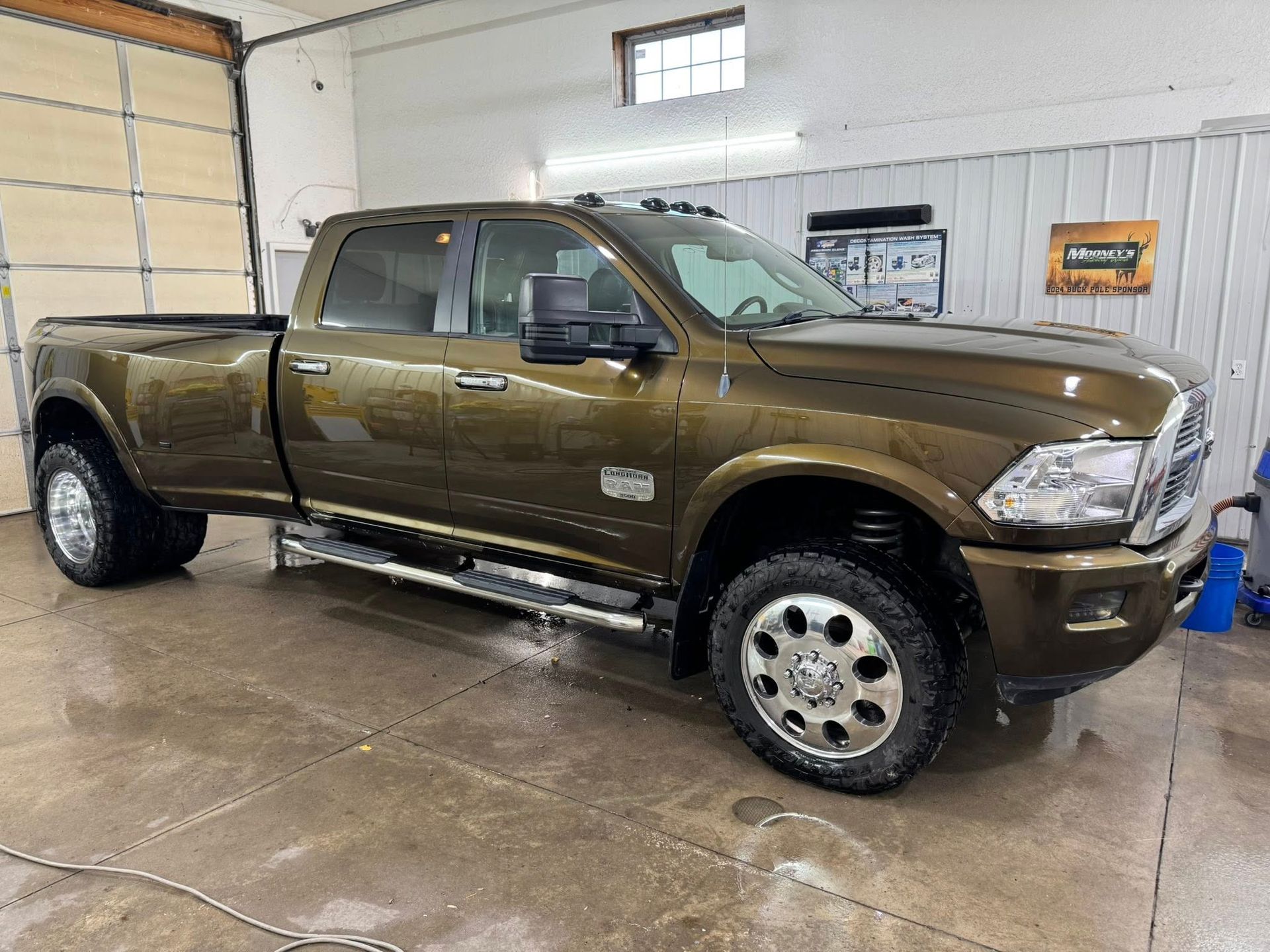 A shiny, dark brown dually pickup truck parked inside a bright, clean garage with concrete floors.