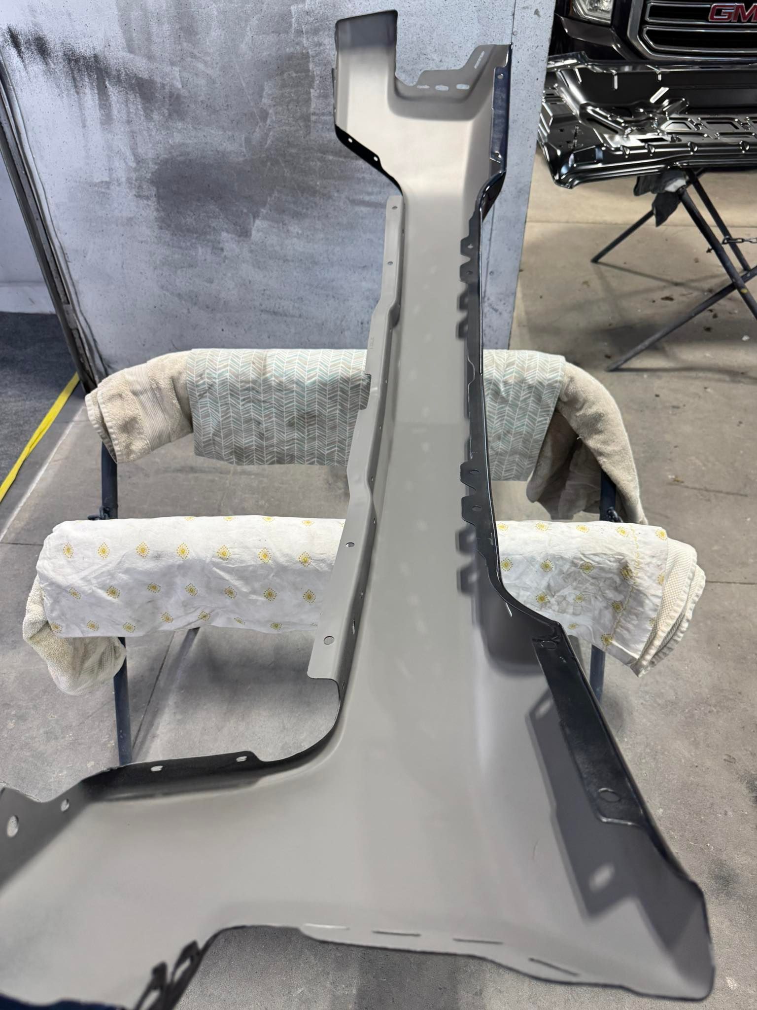 A grey automotive A-pillar body panel rests on a workshop stand, showing its inner side and attachment points.