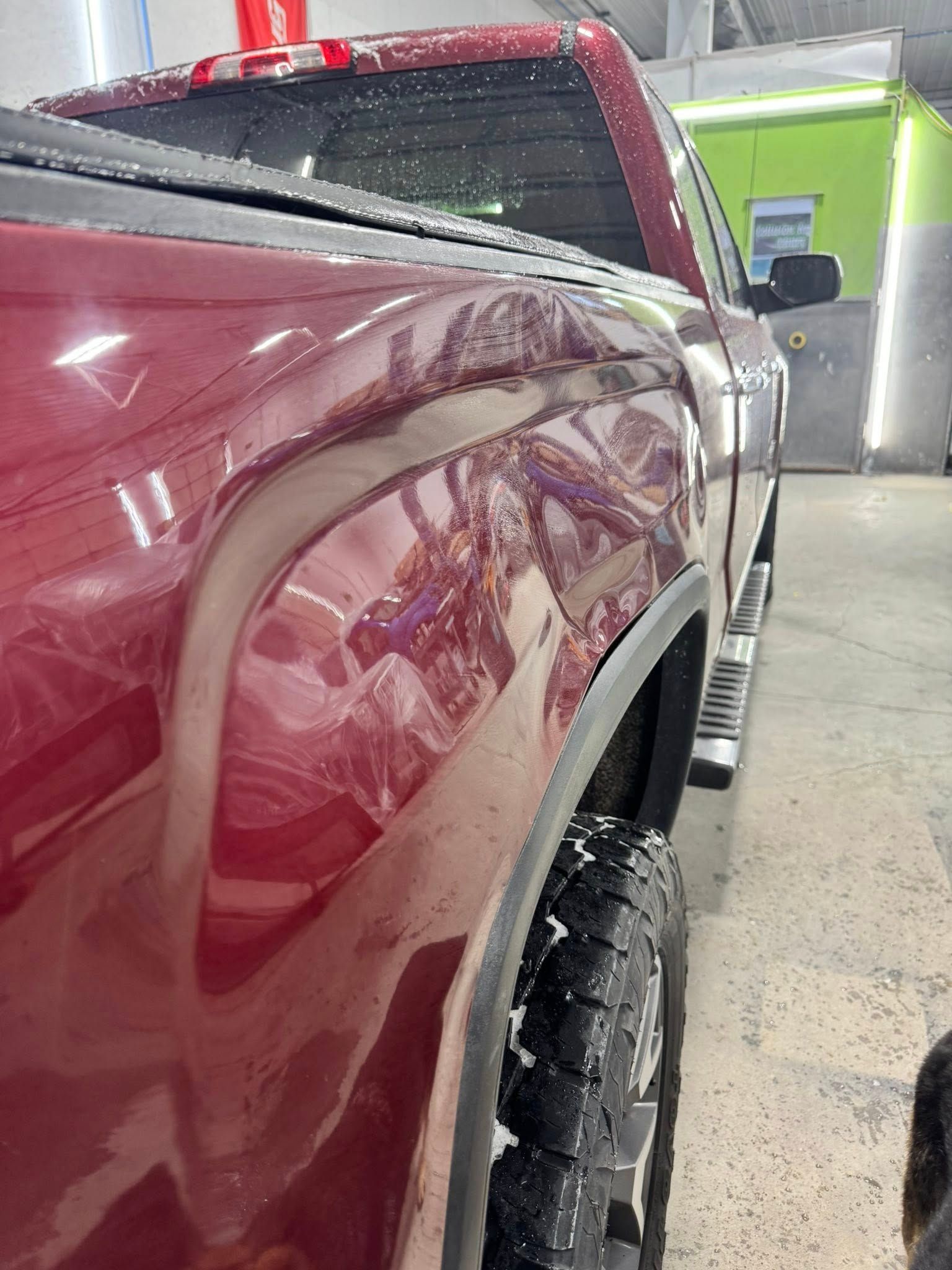 A close-up, angled view of a dented maroon truck bedside in a garage.