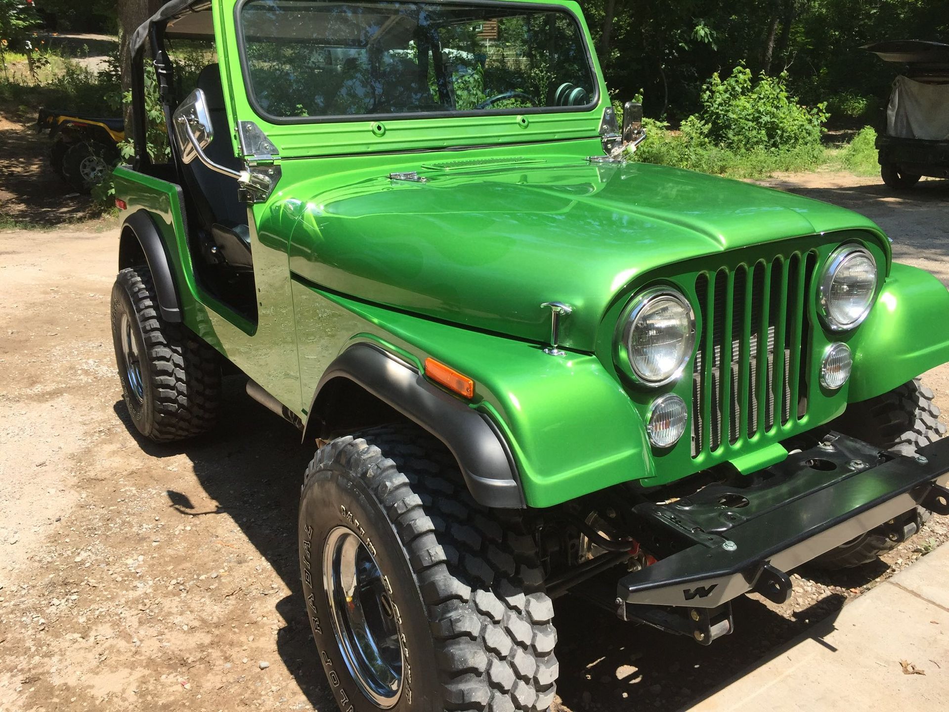 A bright green classic Jeep parked on a dirt lot, featuring black fenders, chrome wheels, and rugged off-road tires.