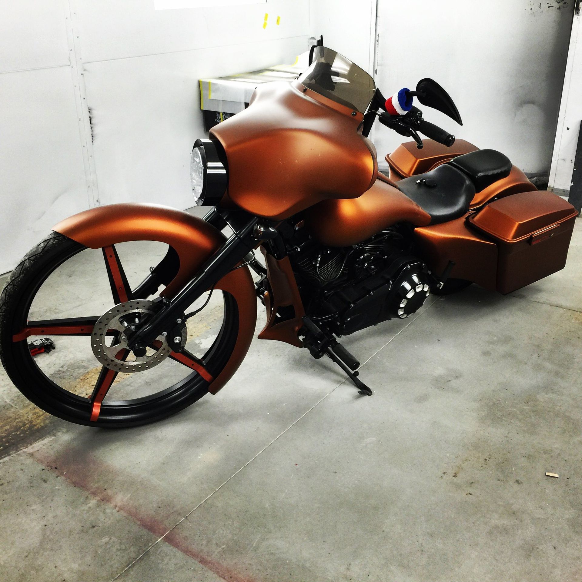 A custom matte copper motorcycle with a large front wheel, black accents, and side storage bags, parked indoors.