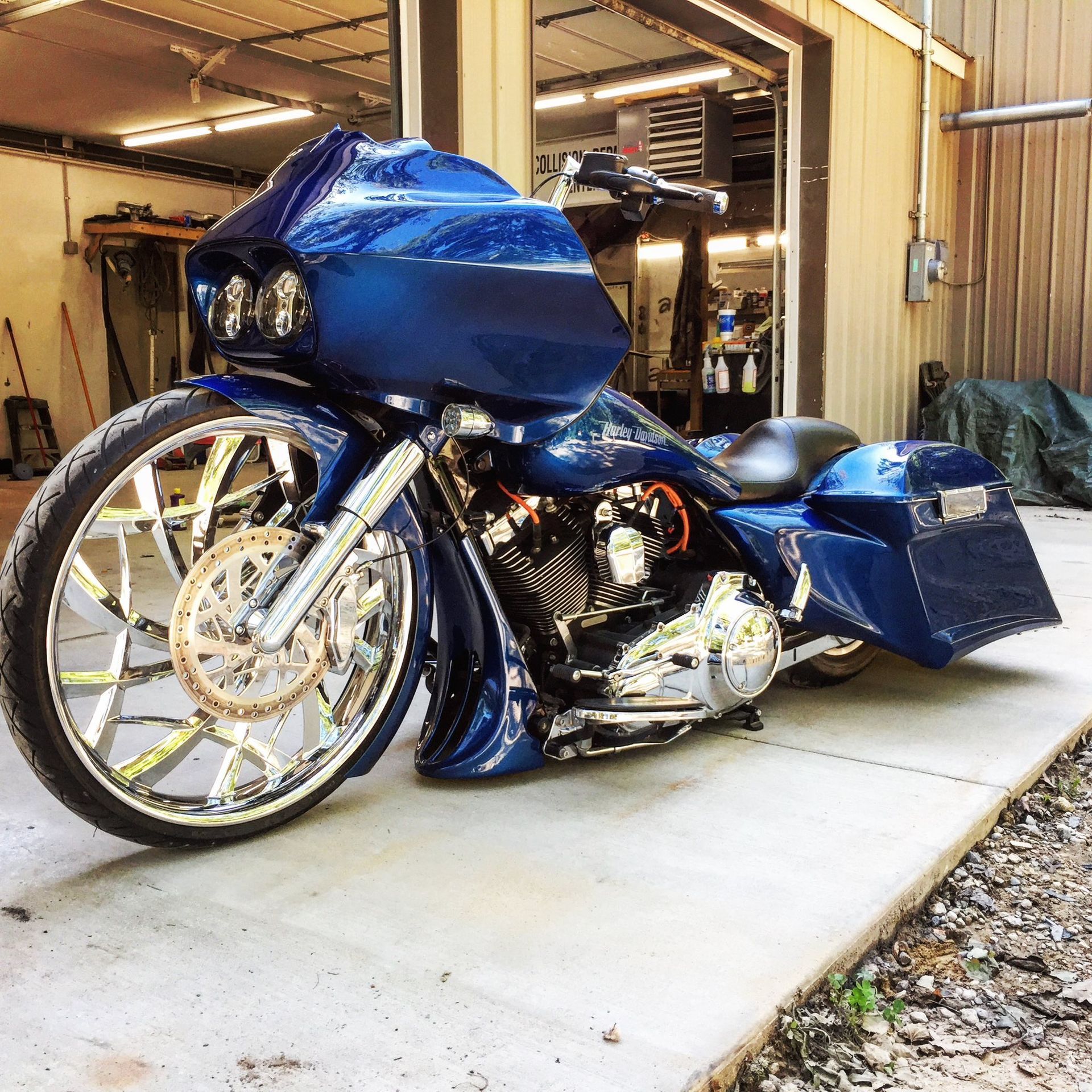 A customized, deep blue touring motorcycle with a large, thin spoked front wheel parked outside a garage.