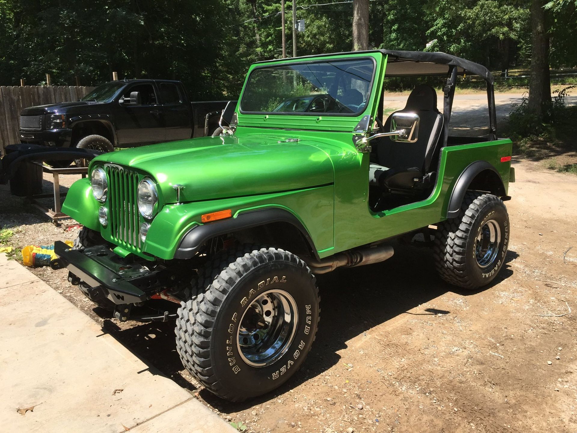 A bright green Jeep with large off-road tires parked on a dirt lot on a sunny day.