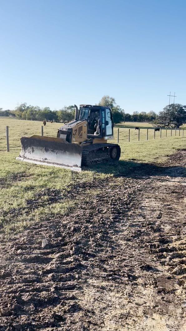 A bulldozer is driving down a dirt road in a field.