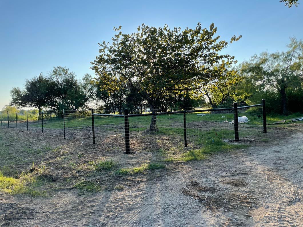 A dirt road with a barbed wire fence and trees in the background.