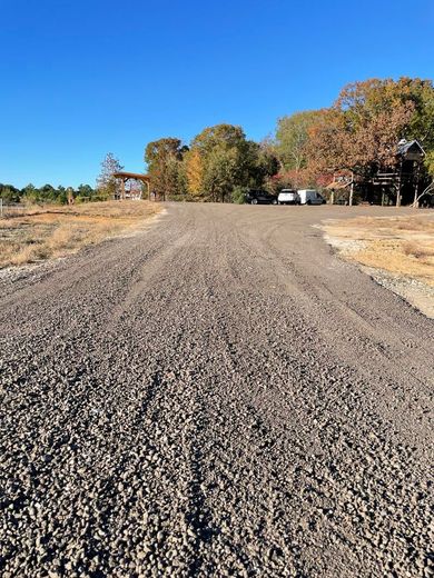 A gravel road going through a field with a house in the background.