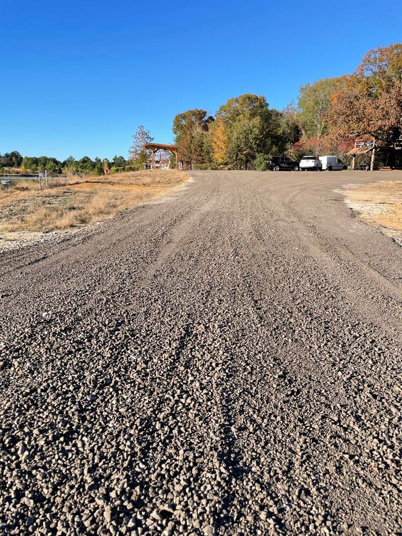 A dirt road with a house in the background and trees on the side.