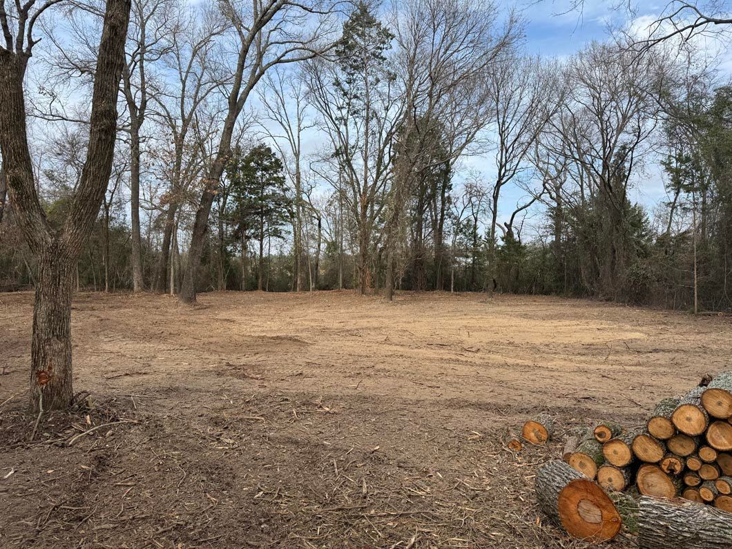 A pile of logs is sitting in the middle of a field with trees in the background.