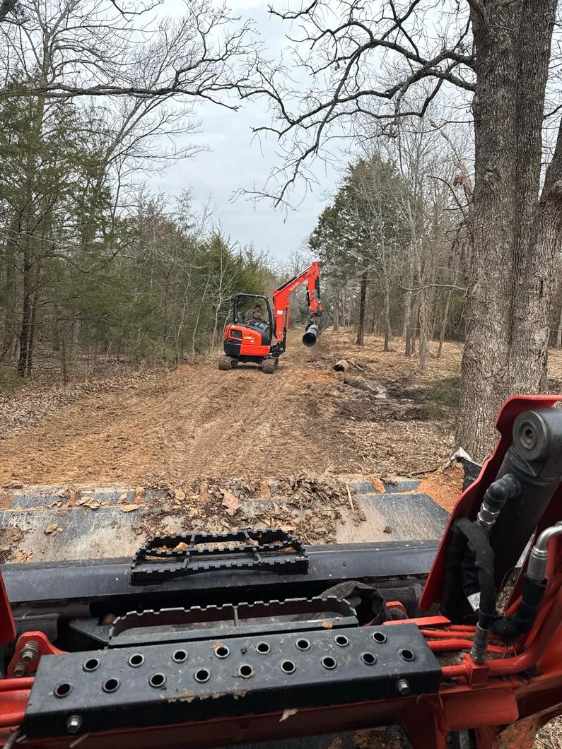 A bulldozer is driving down a dirt road in the woods.