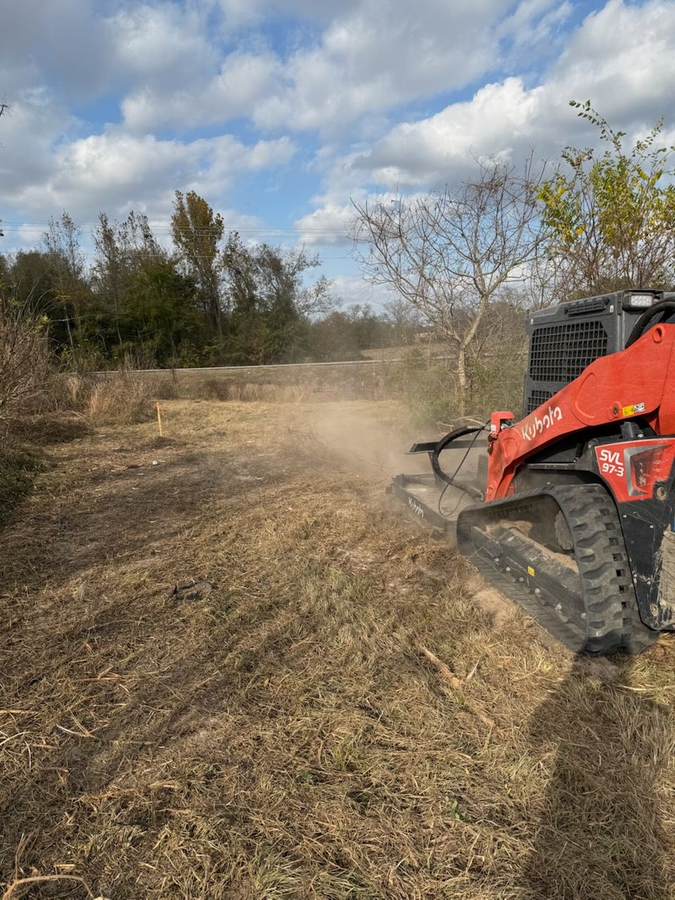 Red skid steer mulching vegetation on a cloudy day.