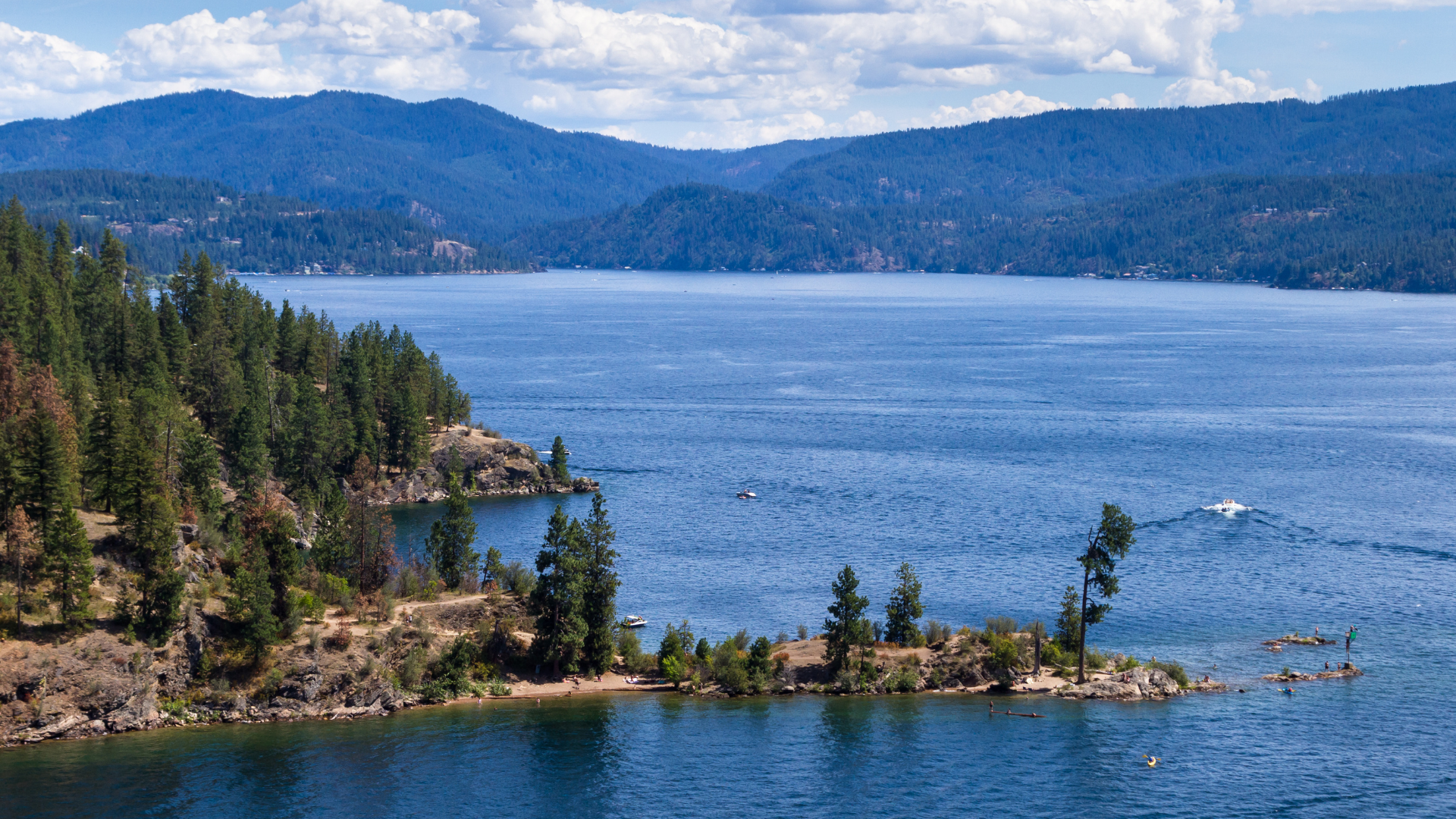 a large body of water with mountains in the background and trees on the shore .