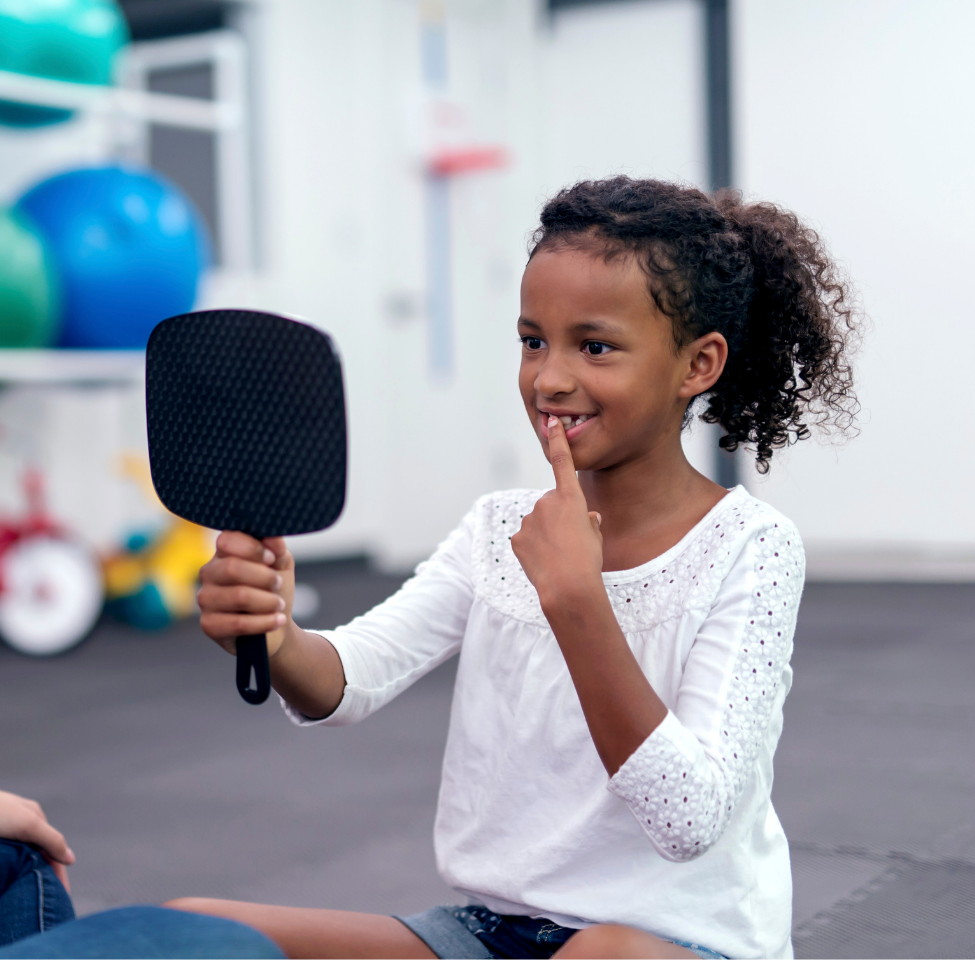 A little girl is looking at herself in a mirror