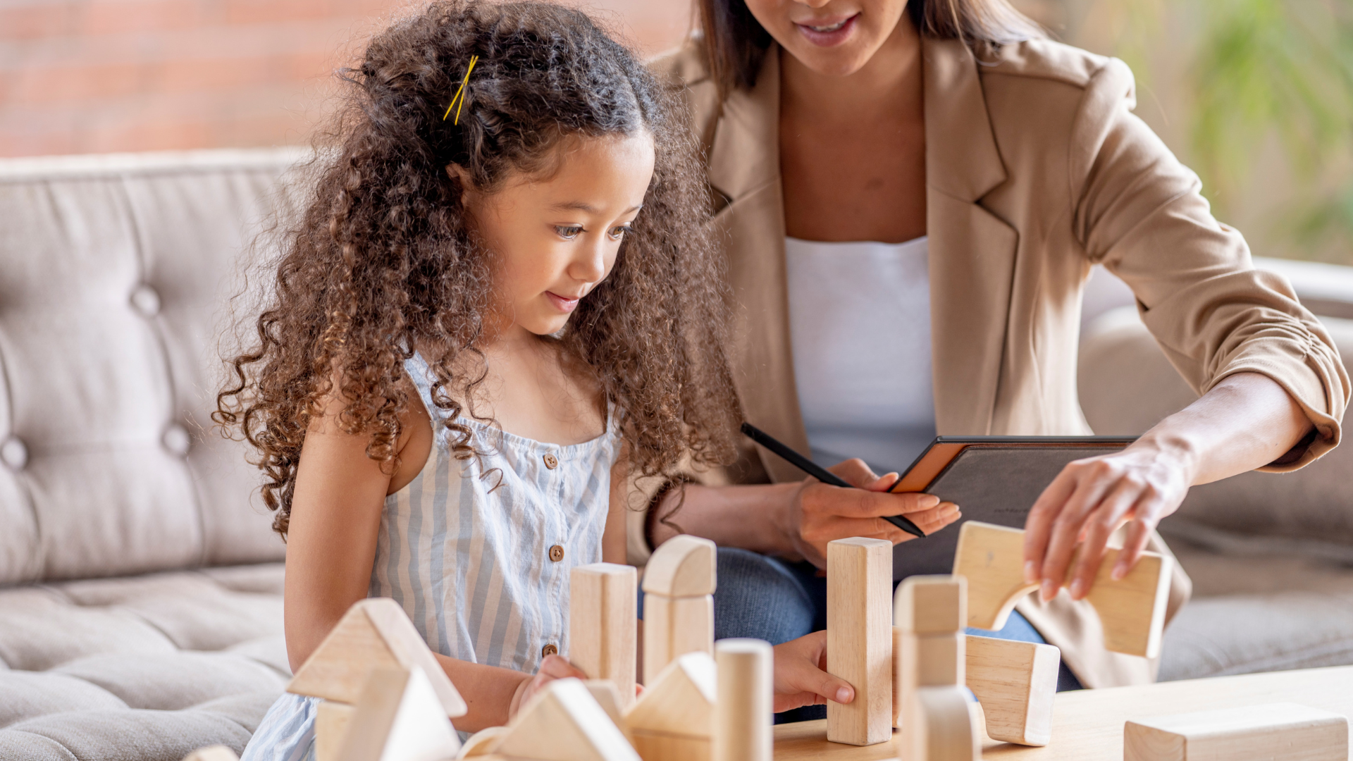 A woman and a little girl are playing with wooden blocks on a couch.