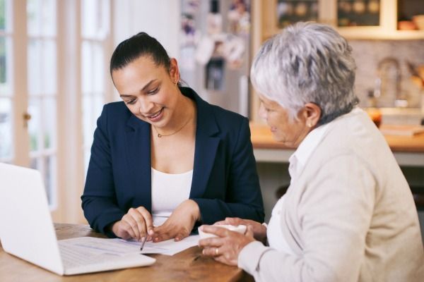 two women are sitting at a table looking at a laptop .
