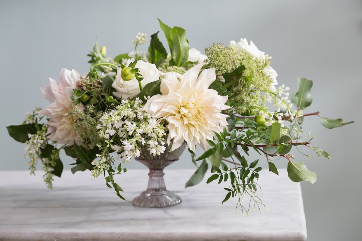 A vase filled with white flowers and greenery is sitting on a table.