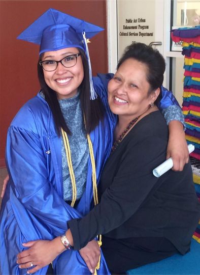 A woman in a graduation cap and gown is hugging another woman