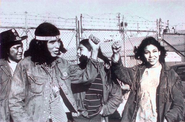 A black and white photo of a group of people standing in front of a fence