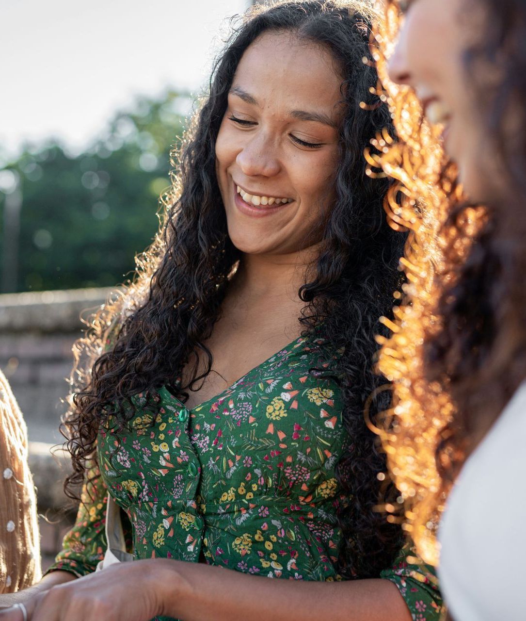 A woman with long curly hair is smiling while holding a glass of wine.