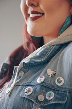 A woman wearing a denim jacket with pins on it.